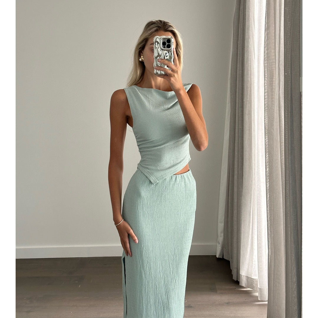Female model online wearing teal tank crop top with high waisted teal textured midi skirt.