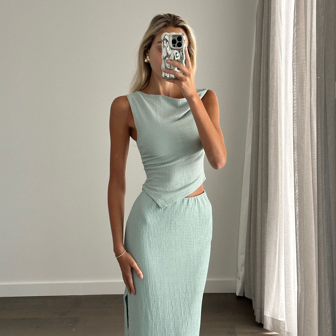 Female model online wearing teal tank crop top with high waisted teal textured midi skirt.