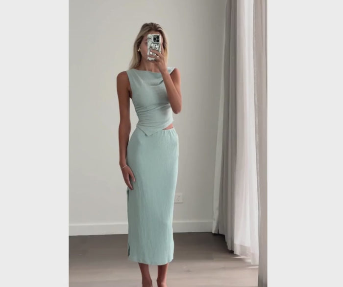 Female model online wearing teal tank crop top with high waisted teal textured midi skirt.