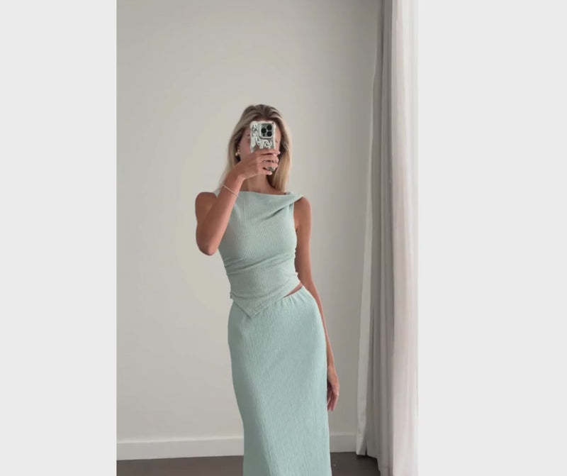 Female model online wearing teal tank crop top with high waisted teal textured midi skirt.