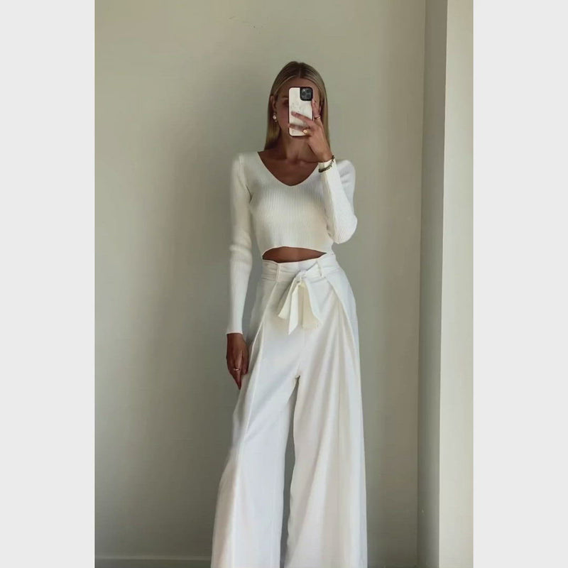 Female model wearing white highwaisted wide leg pants paired with a long sleeve white knit top